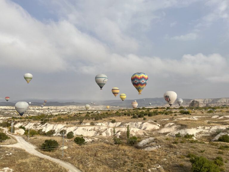 Zahlreiche Heißluftballons steigen über der kargen, hügeligen Landschaft Kappadokiens (Türkei) auf.