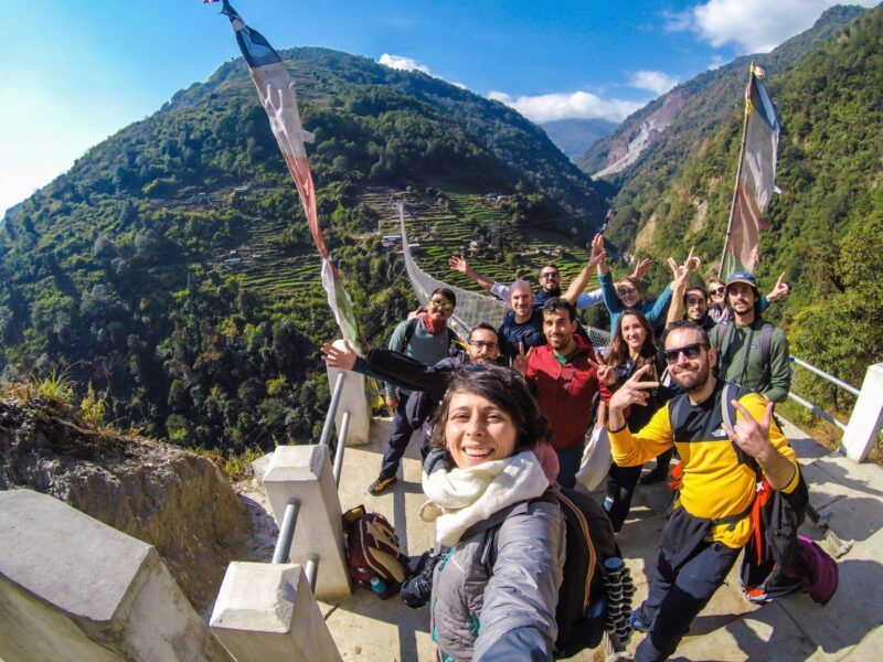Ein fröhliches WeRoad-Gruppenselfie auf einer Hängebrücke in den Bergen Nepals.