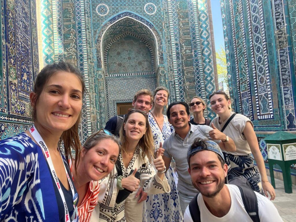 Eine Gruppe von WeRoad-Reisenden macht ein Selfie vor einem prachtvollen, mit blauen Mosaiken verzierten Gebäude in Usbekistan.