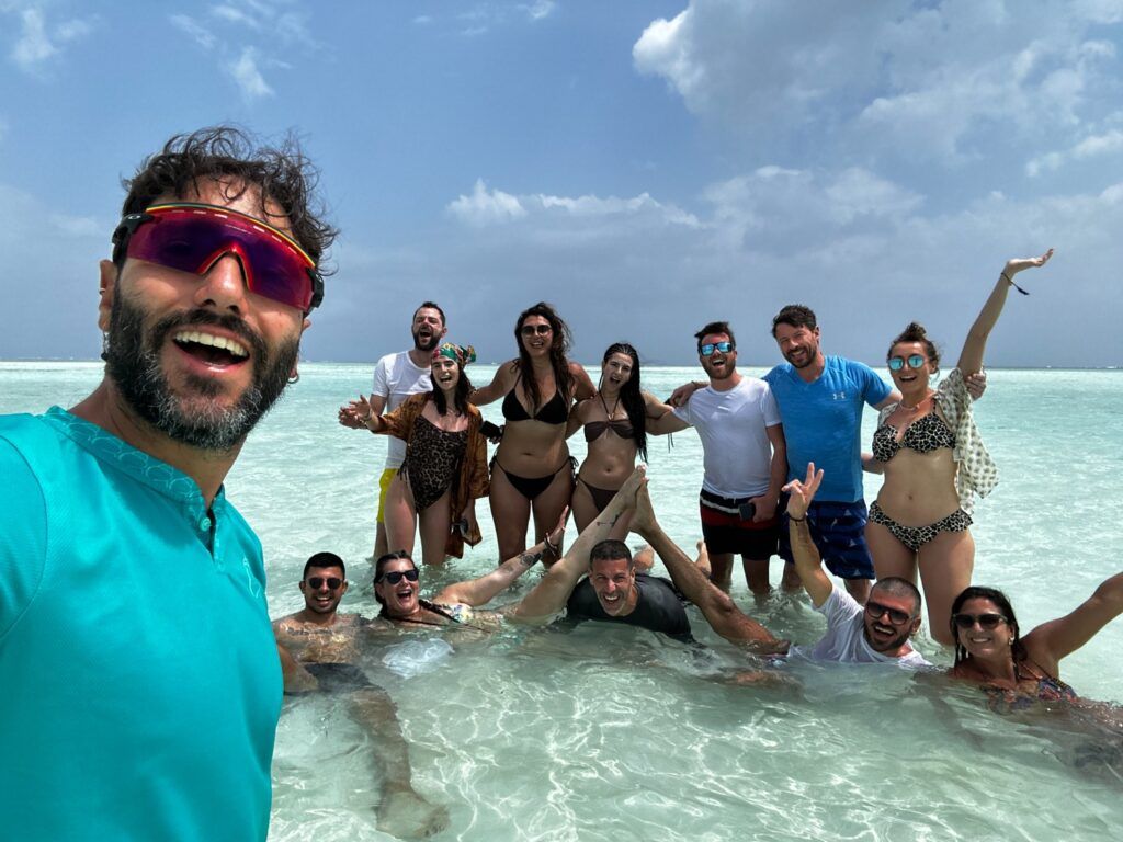 Eine Gruppe fröhlicher WeRoad-Reisender macht ein Selfie im flachen, kristallklaren Wasser vor der Küste Madagaskars