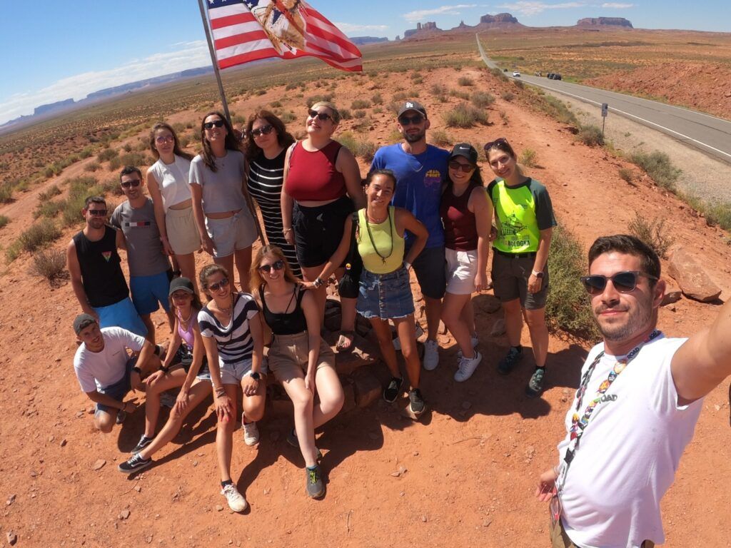 WeRoad-Gruppe macht ein Selfie im Monument Valley vor einer weiten Wüstenlandschaft mit roten Felsen.