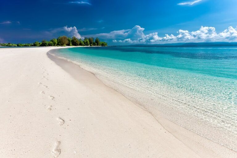 Ein einsamer weißer Sandstrand auf den Philippinen mit Fußabdrücken im Sand und kristallklarem, türkisfarbenem Wasser unter einem blauen Himmel.