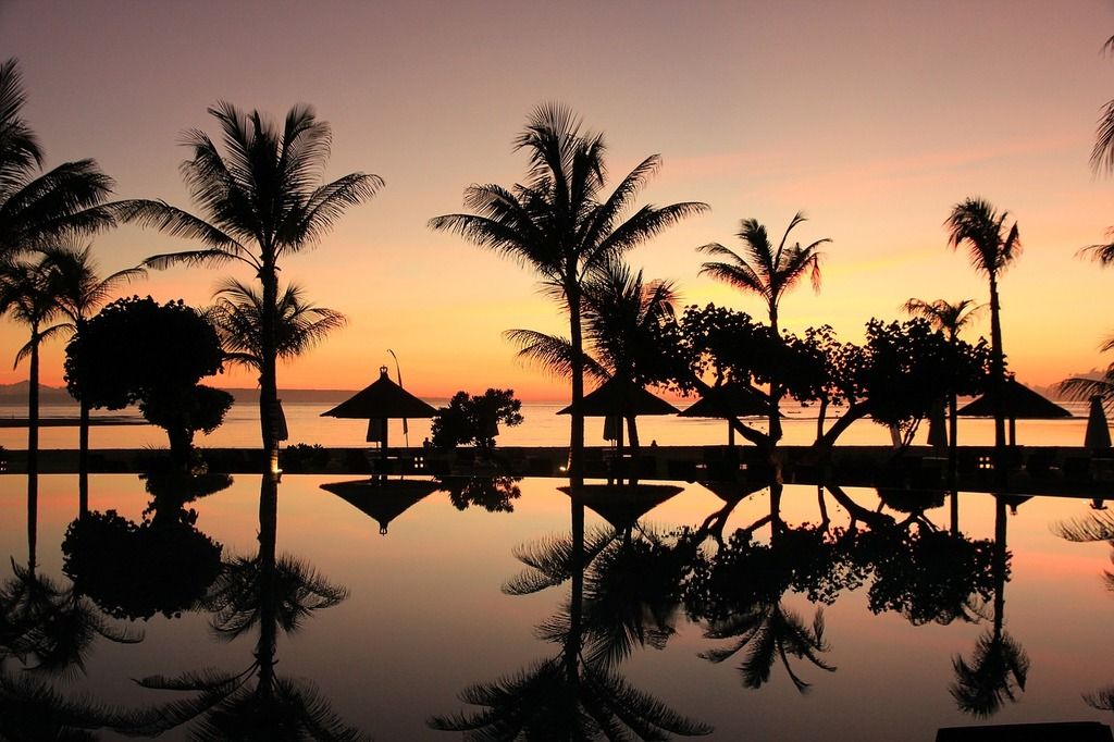 Eine atemberaubende Aussicht auf einen tropischen Sonnenuntergang mit Palmen und ihrem Spiegelbild im Wasser auf Bali.