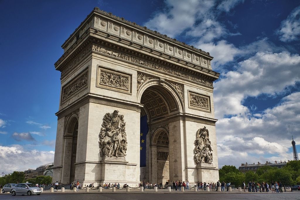 Der Arc de Triomphe auf den Champs-Élysées unter einem bewölkten blauen Himmel.