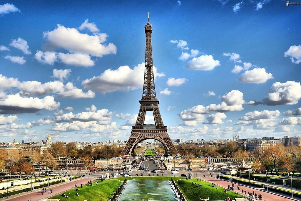 Bild von der Eiffel-Turm in Paris bei blauem Himmel mit Wolken.