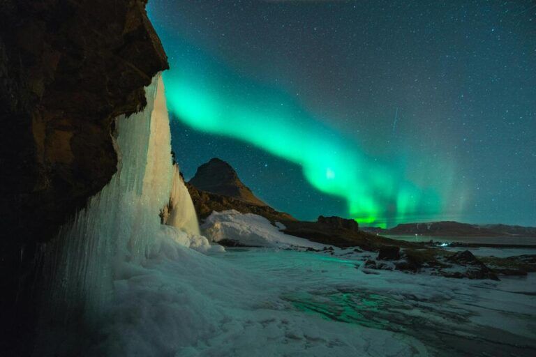Nordlichter über dem Kirkjufell in Island. Eine vereiste Landschaft mit einem Wasserfall unter einem grünen Polarlicht.