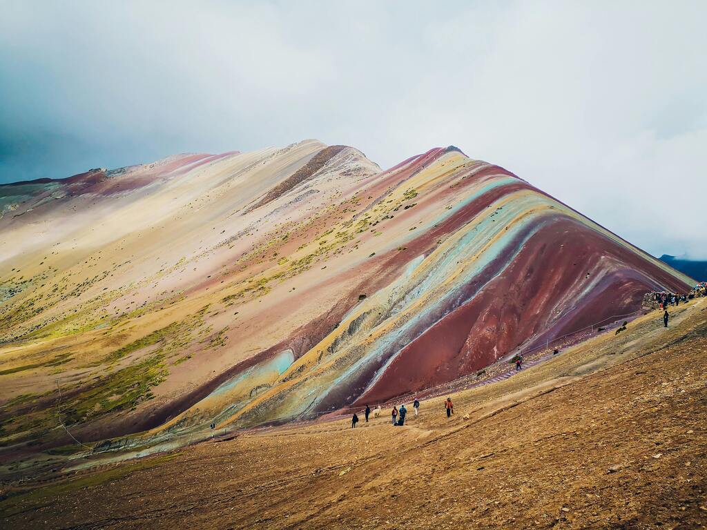Wanderer erklimmen den farbenfrohen Rainbow Mountain (Vinicunca) in den peruanischen Anden bei bewölktem Himmel.