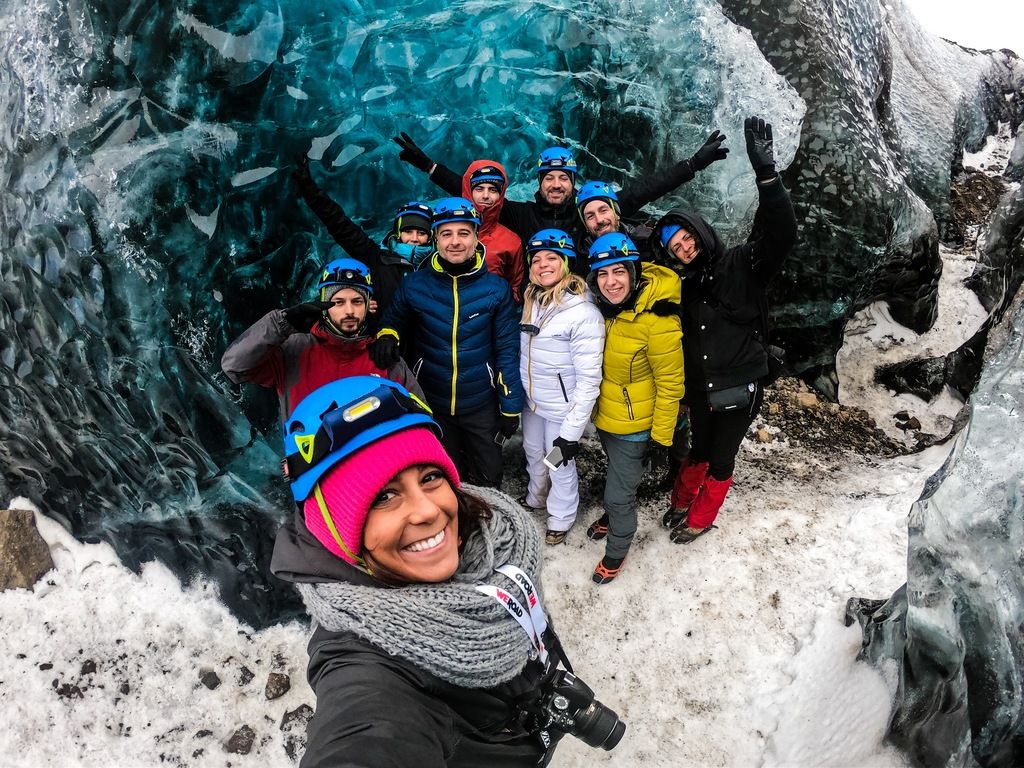 Gruppe WeRoad Reisender macht Selfie in leuchtend blauer Eishöhle in Island.