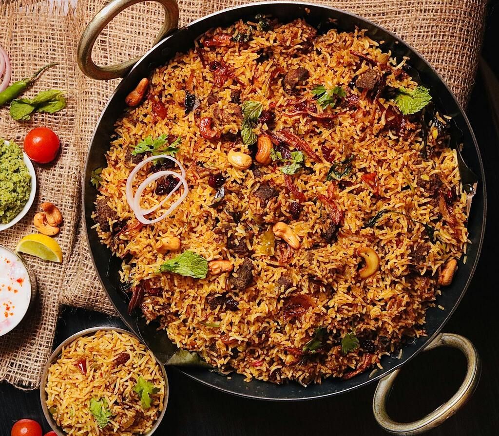 Aromatisches Biryani mit Nüssen, Rosinen und frischen Kräutern, in einer traditionellen Servierpfanne – ein ikonisches Reisgericht der indischen Küche.