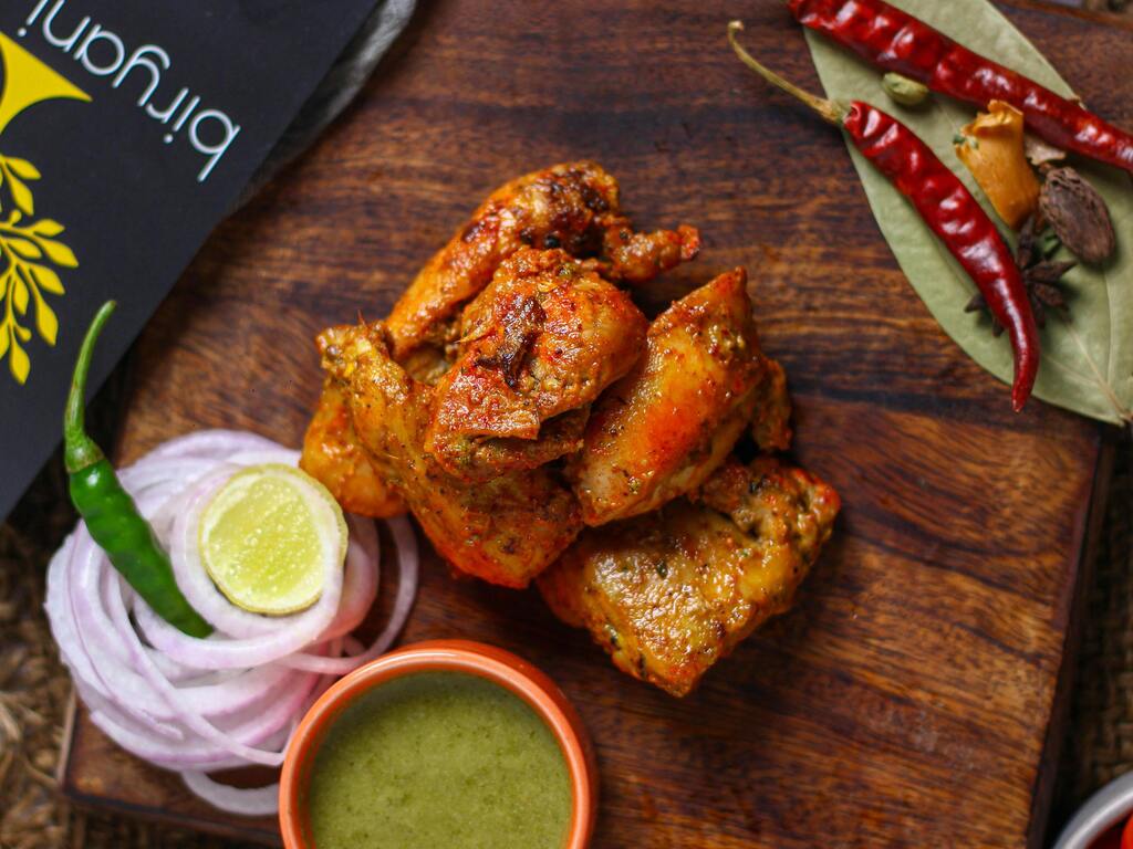 Würzig mariniertes Tandoori-Hähnchen mit Limetten, Zwiebeln und Chutney, serviert auf einem Holzbrett – ein Klassiker von indischem Essen.