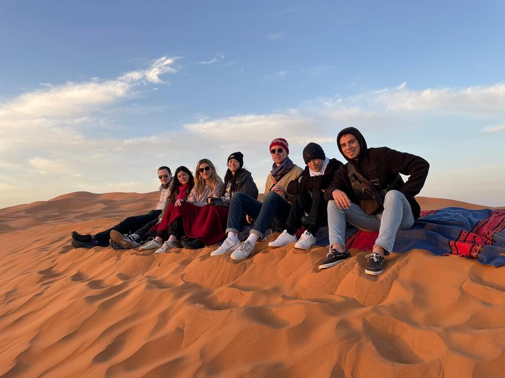 WeRoad-Gruppenreise in die Sahara-Wüste, Reisende sitzen auf den Sanddünen bei Sonnenuntergang.