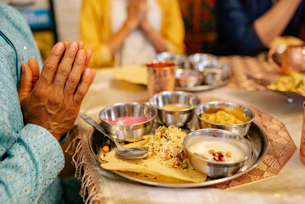 Ein traditionelles indisches Thali mit Reis, Curry und Chutney, serviert auf einem Tisch mit betenden Händen – ein Symbol für indisches Essen.