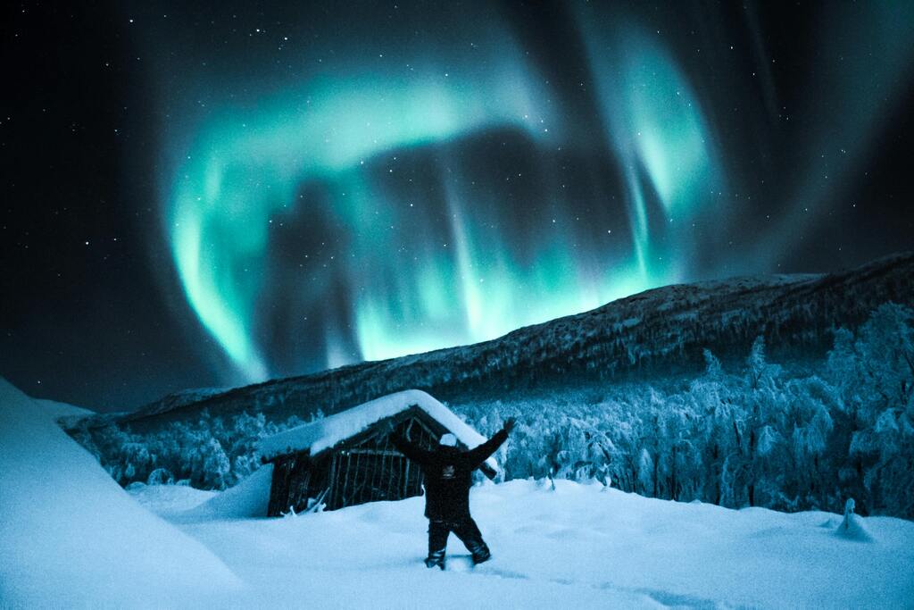 Nordlichter in einer verschneiten Landschaft mit einer Hütte im Vordergrund