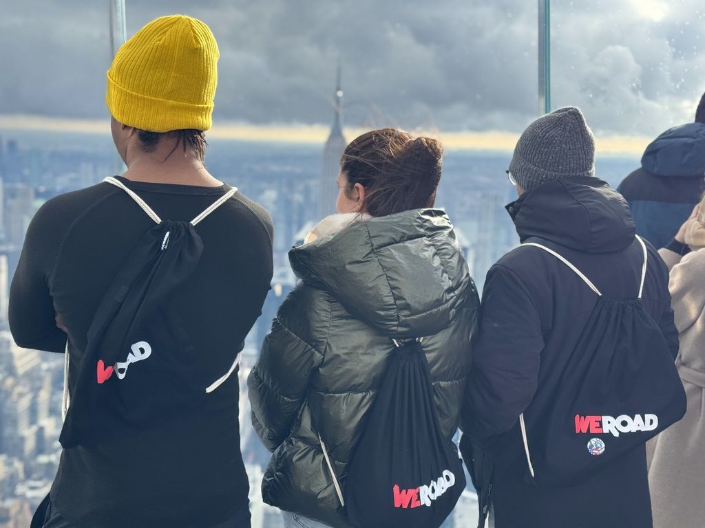 Drei WeRoad Reisende mit Rucksäcken blicken auf die Skyline von New York