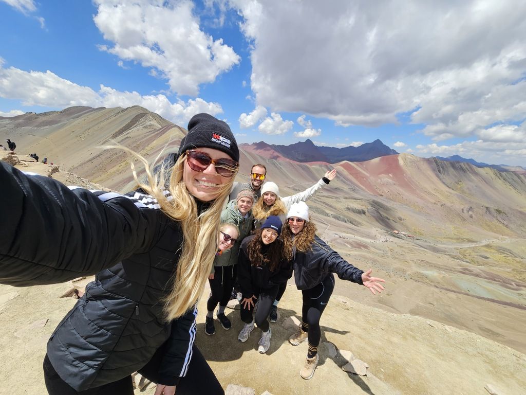 WeRoad Gruppe auf dem Rainbow Mountain in Peru, posierend vor der bunten Berglandschaft