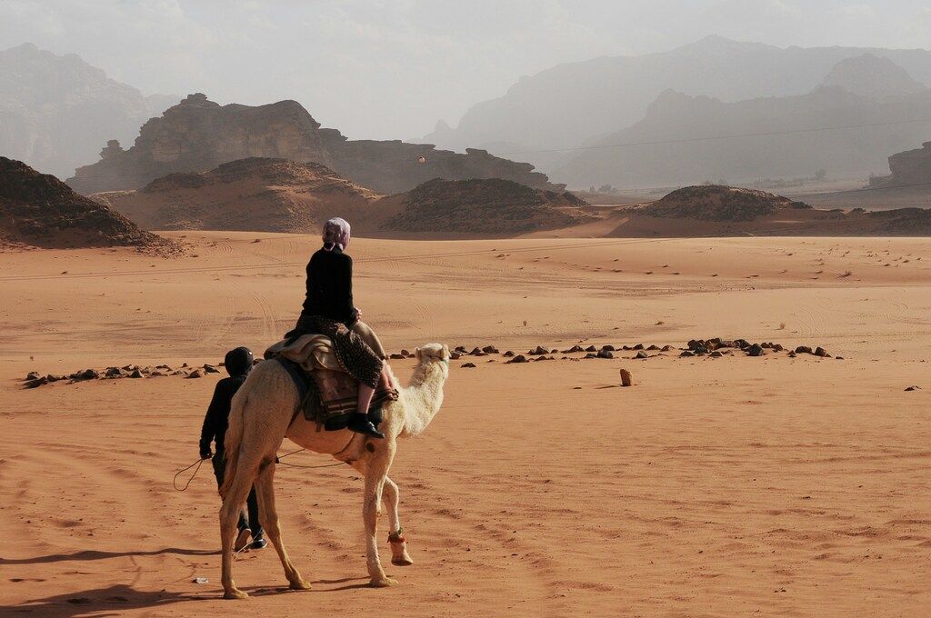 Touristen auf einem Kamel im Wadi Rum, Jordanien, mit Blick auf die weite Wüstenlandschaft