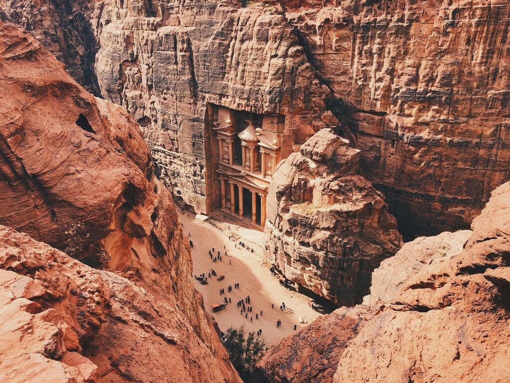 Blick von oben auf Al-Khazneh, das Schatzhaus von Petra, eingebettet in rote Felswände in Jordanien