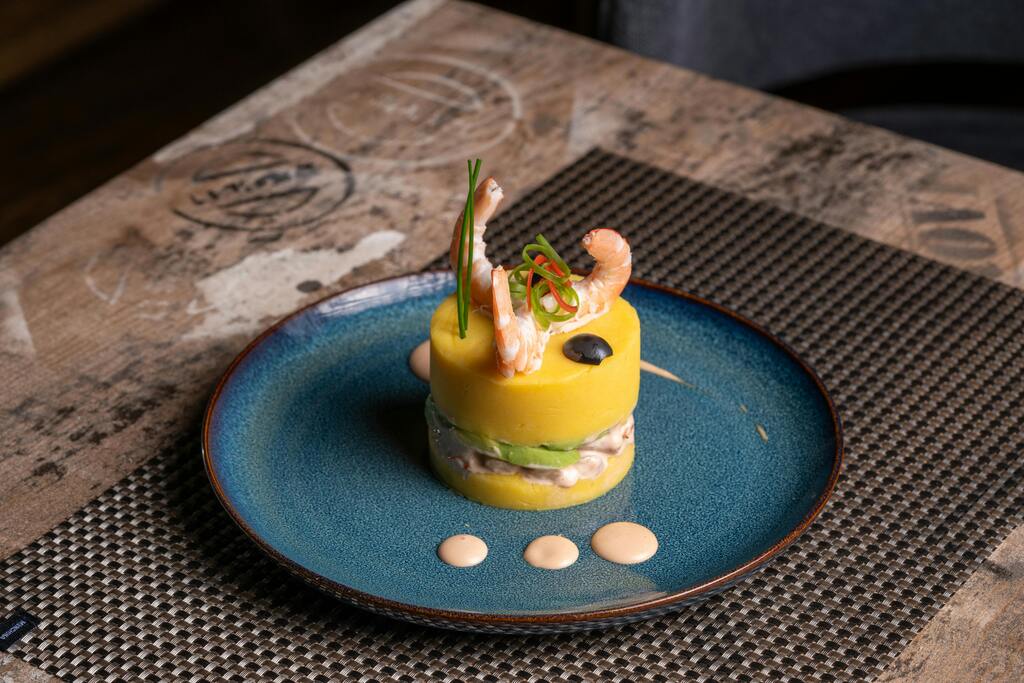 Causa Rellena mit Garnelen, Avocado und Oliven auf einem blauen Teller angerichtet