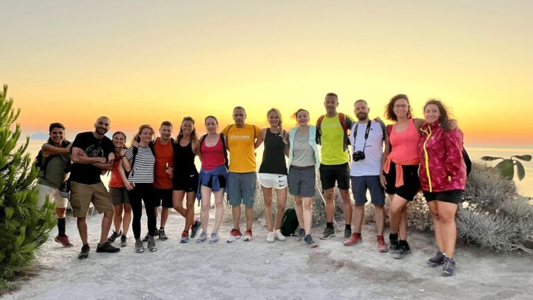 Eine große Gruppe lächelnder Reisender posiert bei Sonnenuntergang im Freien.