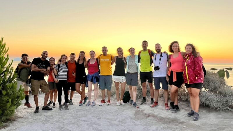 Eine große Gruppe lächelnder Reisender posiert bei Sonnenuntergang im Freien.