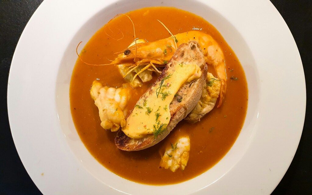  Französische Bouillabaisse mit Garnelen und Brot in einer weißen Schüssel.