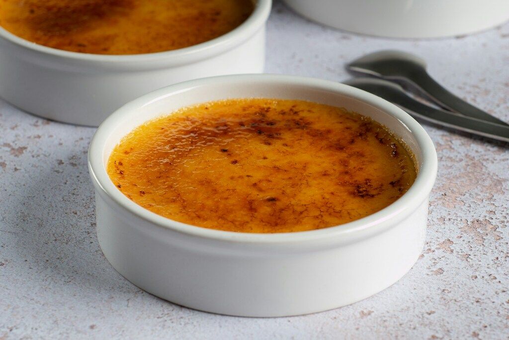Crème brûlée in weißen Ramekins mit karamellisierter Zuckerschicht.