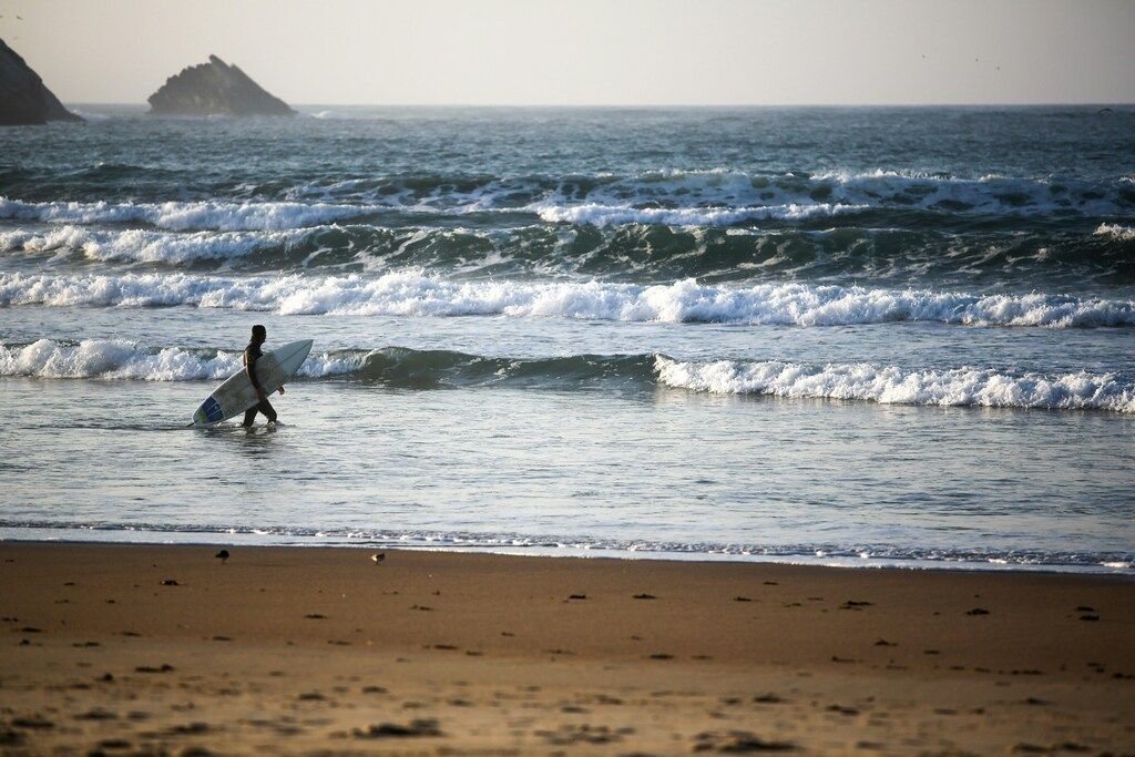 Surfer mit Brett am Strand ins Wasser gehend.