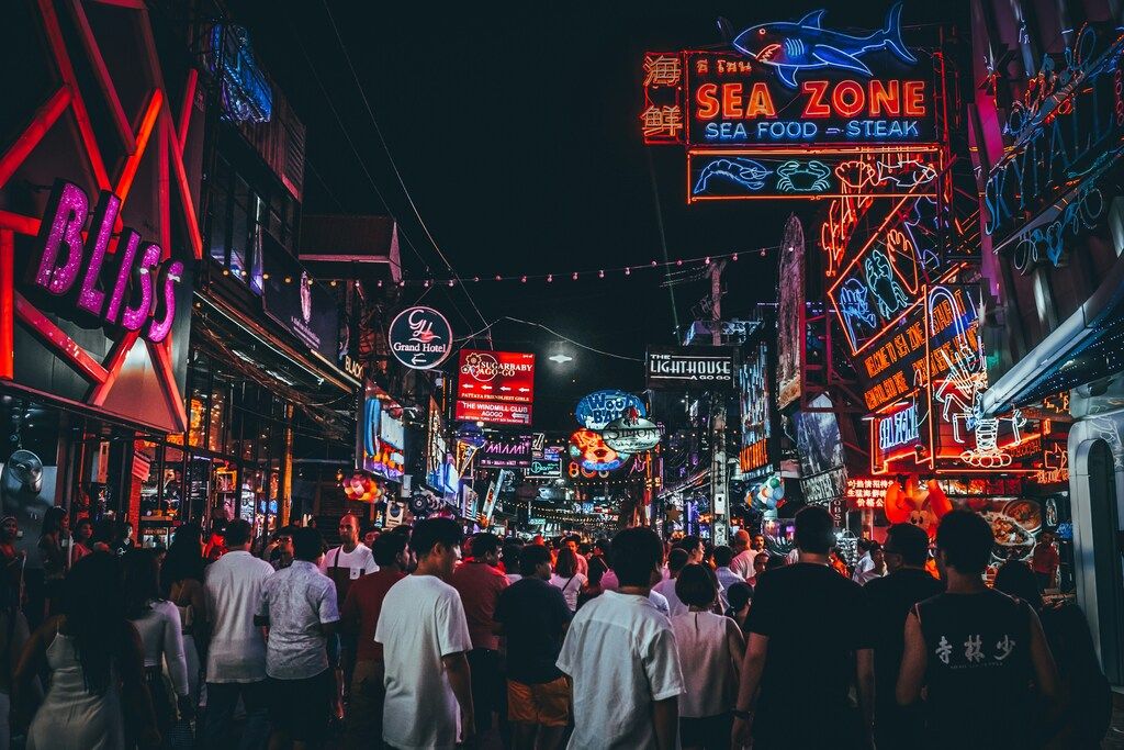 Lebhafte Nachtstraße in Thailand mit bunten Neonlichtern, Restaurants und Menschenmengen.