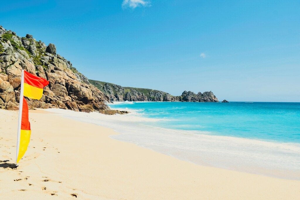 Weitläufiger Sandstrand von Porthcurno in Cornwall mit Felsen und türkisblauem Meer.