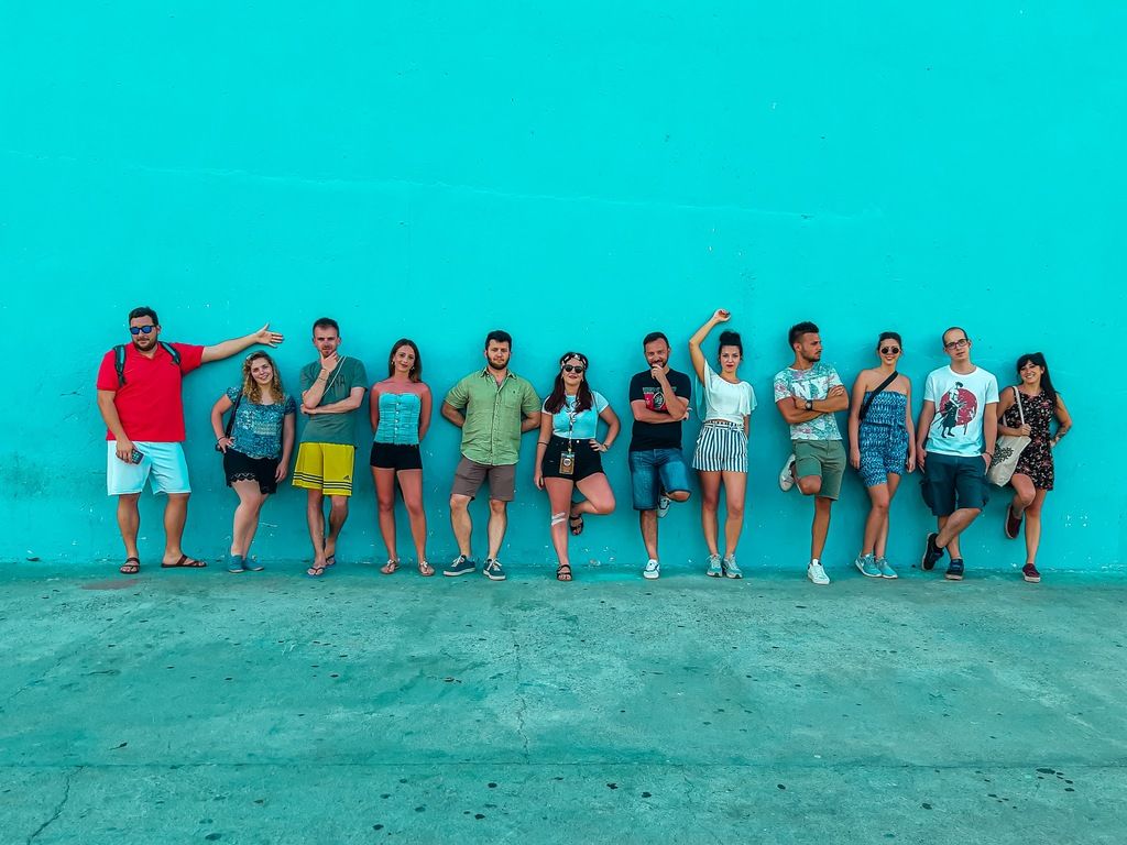 Eine fröhliche Reisegruppe von jungen Erwachsenen posiert vor einer leuchtend blauen Wand im Urlaub.