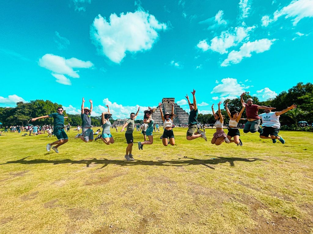 Gruppe junger Reisender springt synchron vor der Pyramide von Chichén Itzá in Mexiko.