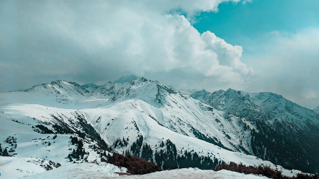 Schneebedeckte Berge unter dramatischem Himmel – Winterlandschaft in den kirgisischen Alpen.
