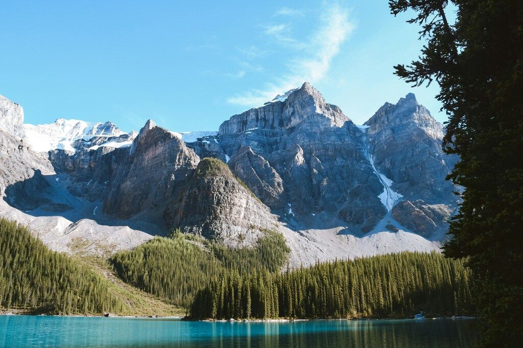 Kristallklarer Bergsee mit Blick auf schneebedeckte Felsgipfel und dichten Nadelwald