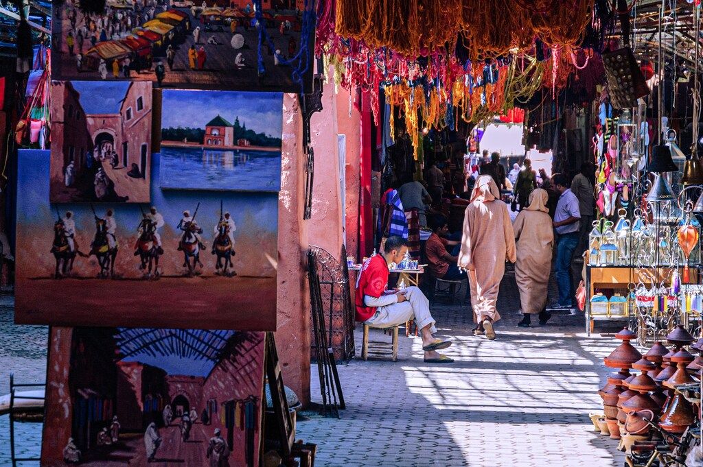 Traditioneller Souk in Marrakesch mit bunten Gemälden, Teppichen und handgefertigten Waren.