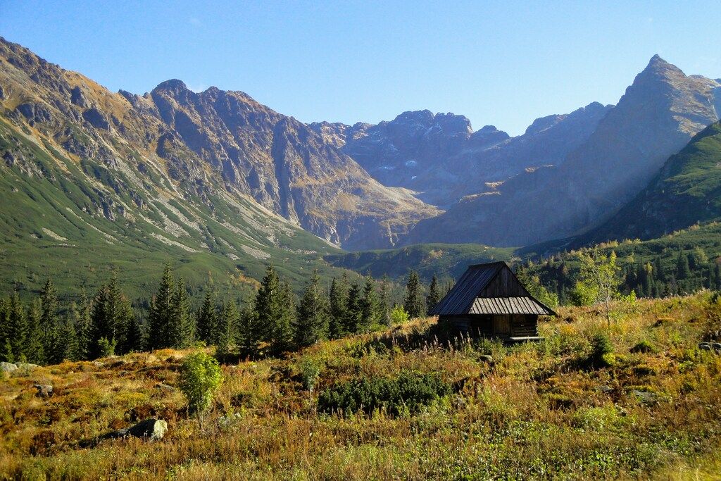 Rustikale Holzhütte in einem grünen Tal, umgeben von imposanten Bergketten