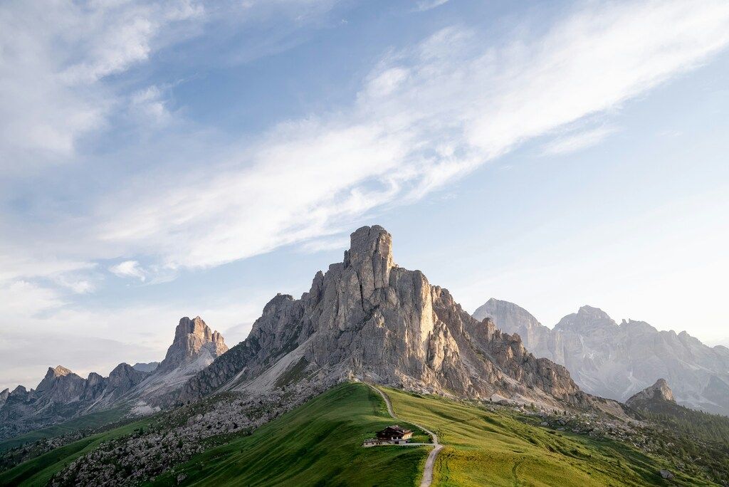 Die majestätischen Gipfel der Dolomiten über einer grünen Alm mit einer kleinen Berghütte unter einem hellen Himmel.
