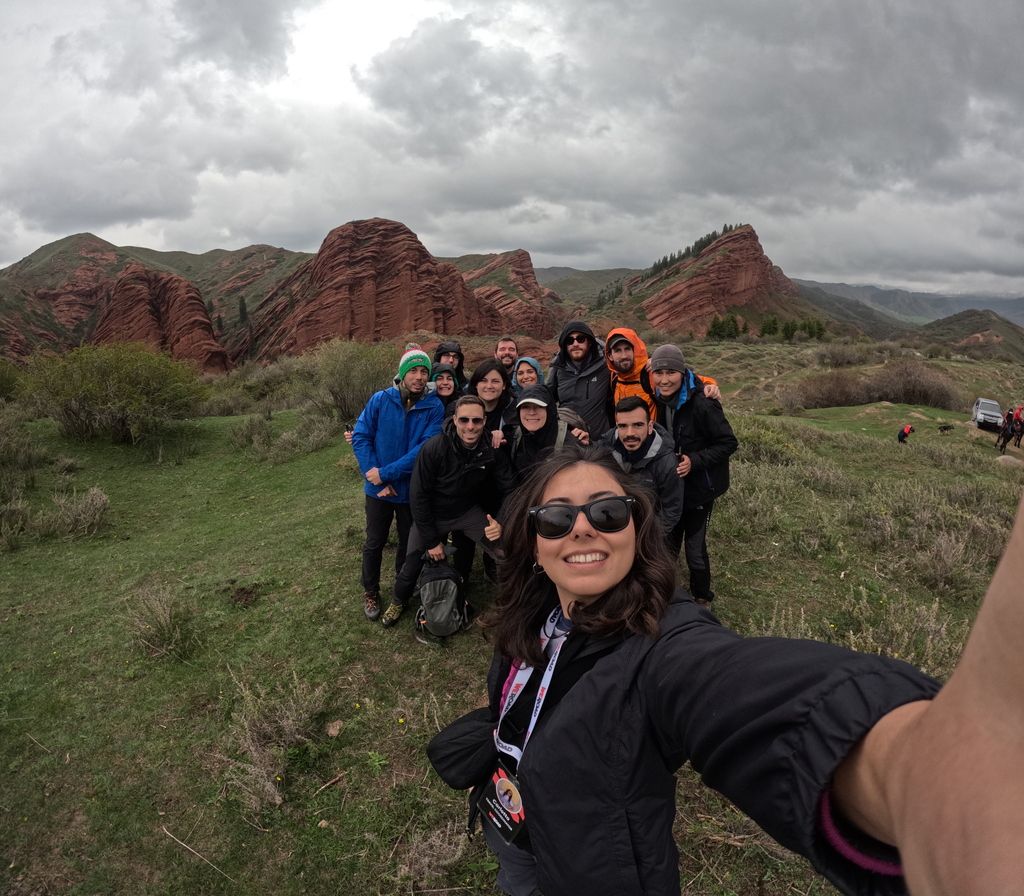 Fröhliche WeRoad-Reisegruppe macht ein Selfie vor den roten Felsformationen in Kirgisistan