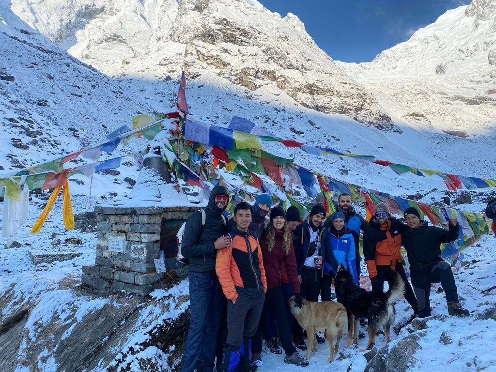 Eine Gruppe von WeRoad-Reisenden posiert im Schnee vor einem buddhistischen Schrein mit bunten Gebetsfahnen im nepalesischen Himalaya.