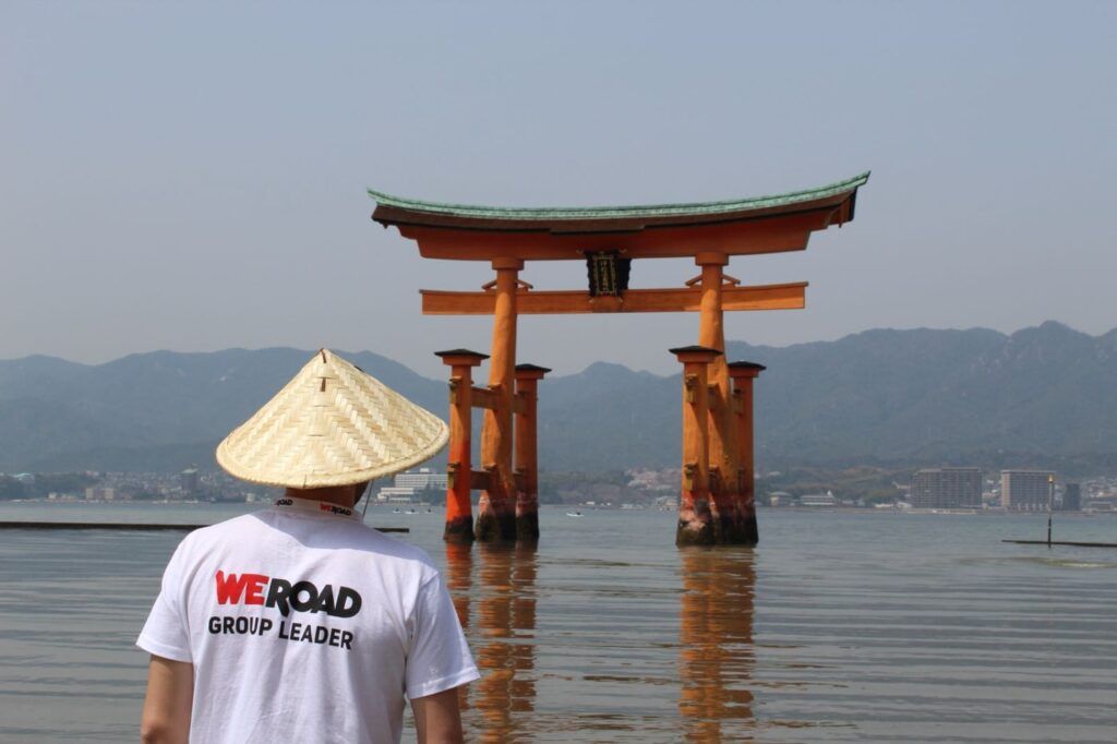 Ein WeRoad-Gruppenleiter in der Nähe des schwimmenden Torii-Tors des Itsukushima-Schreins in Japan.