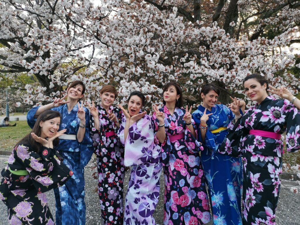 WeRoad-Reisegruppe in Japan posiert vor Kirschblüten, gekleidet in traditionelle Kimonos.