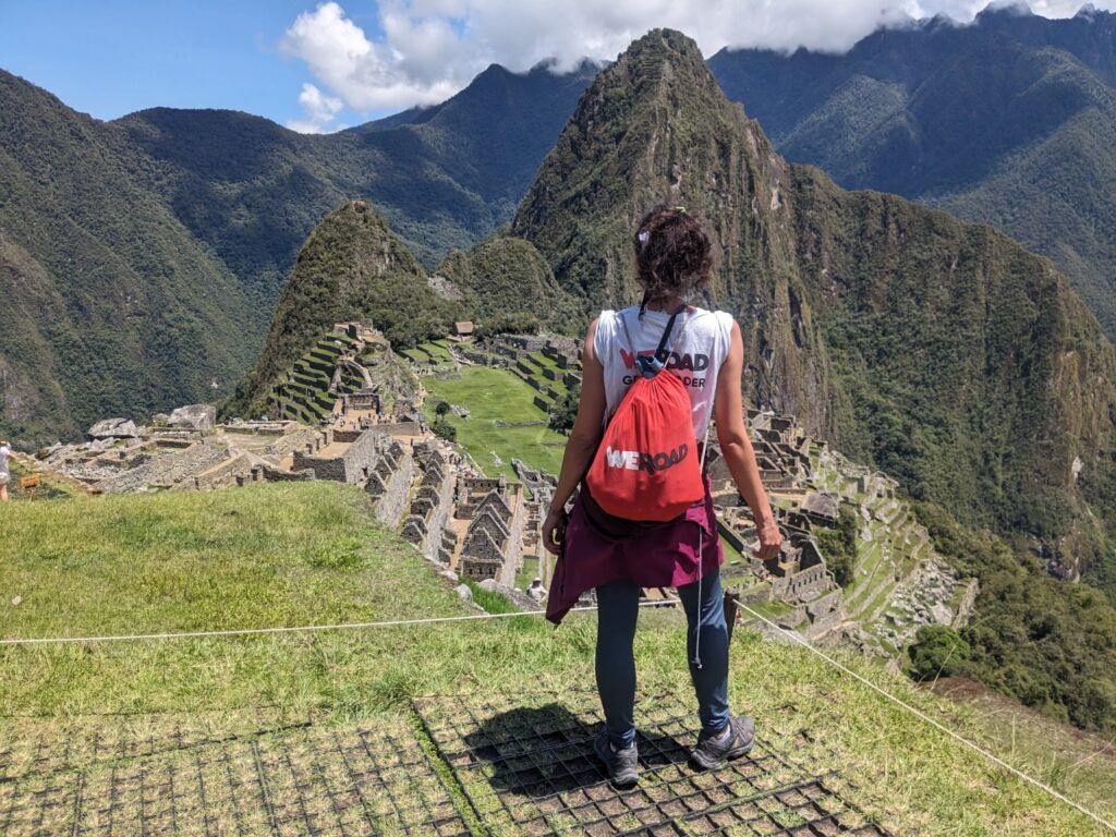 WeRoad-Reisende blickt mit rotem Rucksack auf die Ruinen von Machu Picchu und Huayna Picchu.