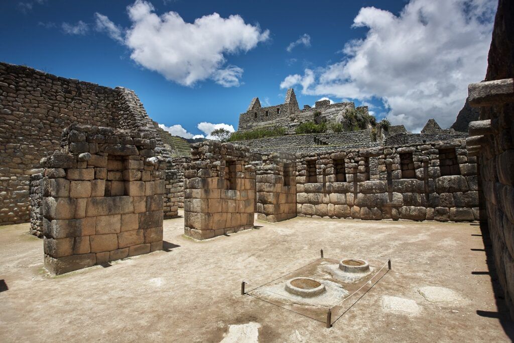 Historische Steinmauern und Höfe innerhalb der Inka-Zitadelle Machu Picchu unter blauem Himmel.