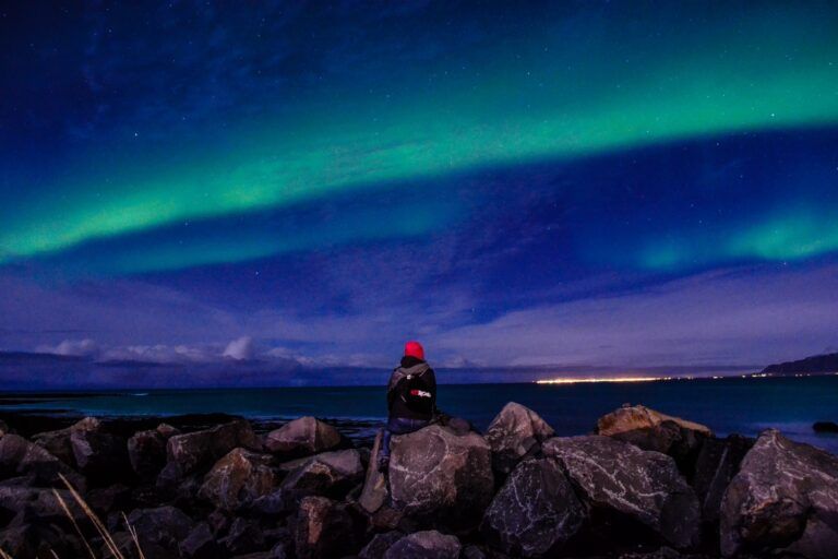 Reisender beobachtet grüne Nordlichter (Aurora Borealis) über dem Meer in Island.