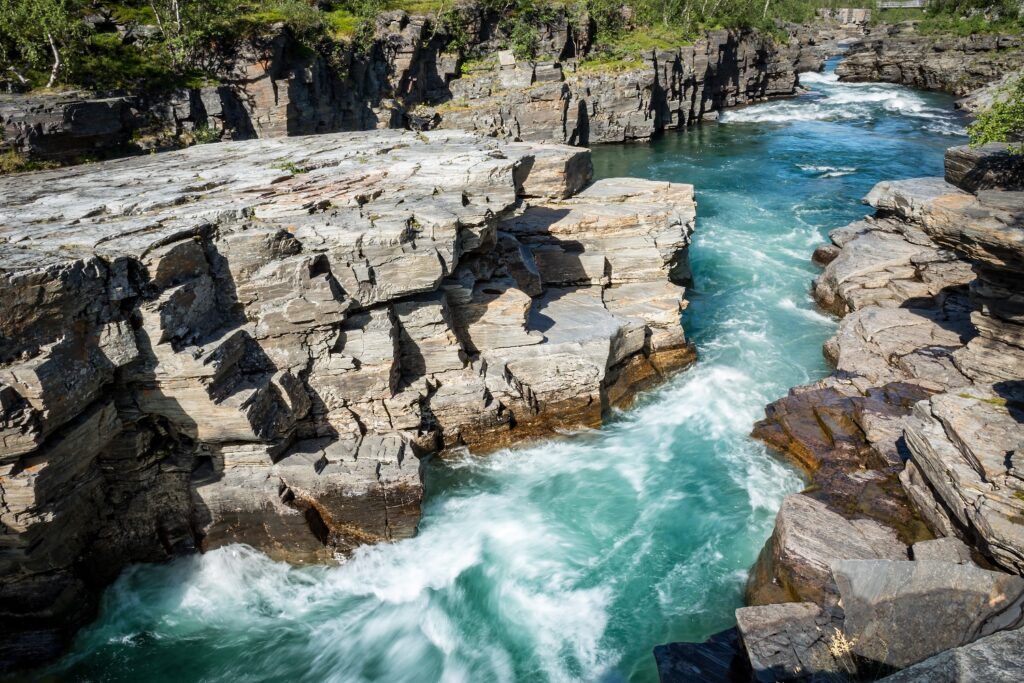 Türkisfarbenes Wildwasser fließt reißend durch eine steile Felsenschlucht (Abisko).