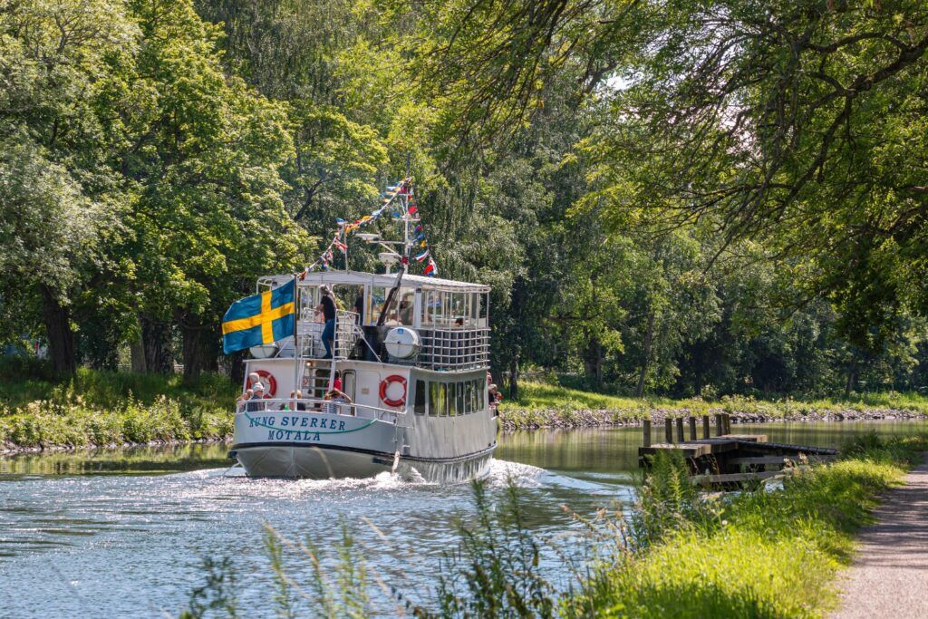 Historisches Passagierschiff Väg SVERKER auf dem Götakanal, umgeben von grüner Ufervegetation.