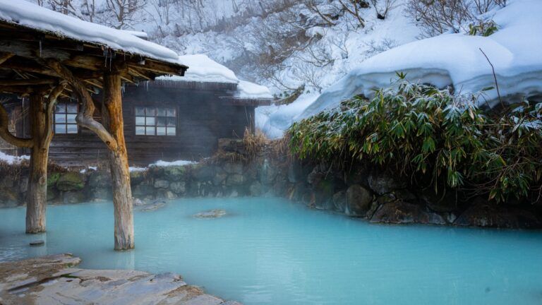 Ein traditioneller japanischer Onsen im Winter mit dampfendem blauem Thermalwasser,