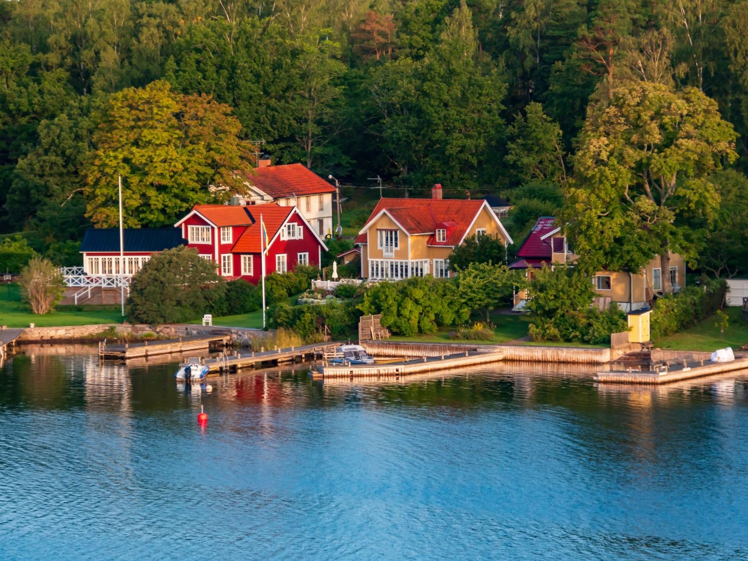 Idyllische rote und gelbe Holzhäuser mit Bootsstegen an der Schärenküste.