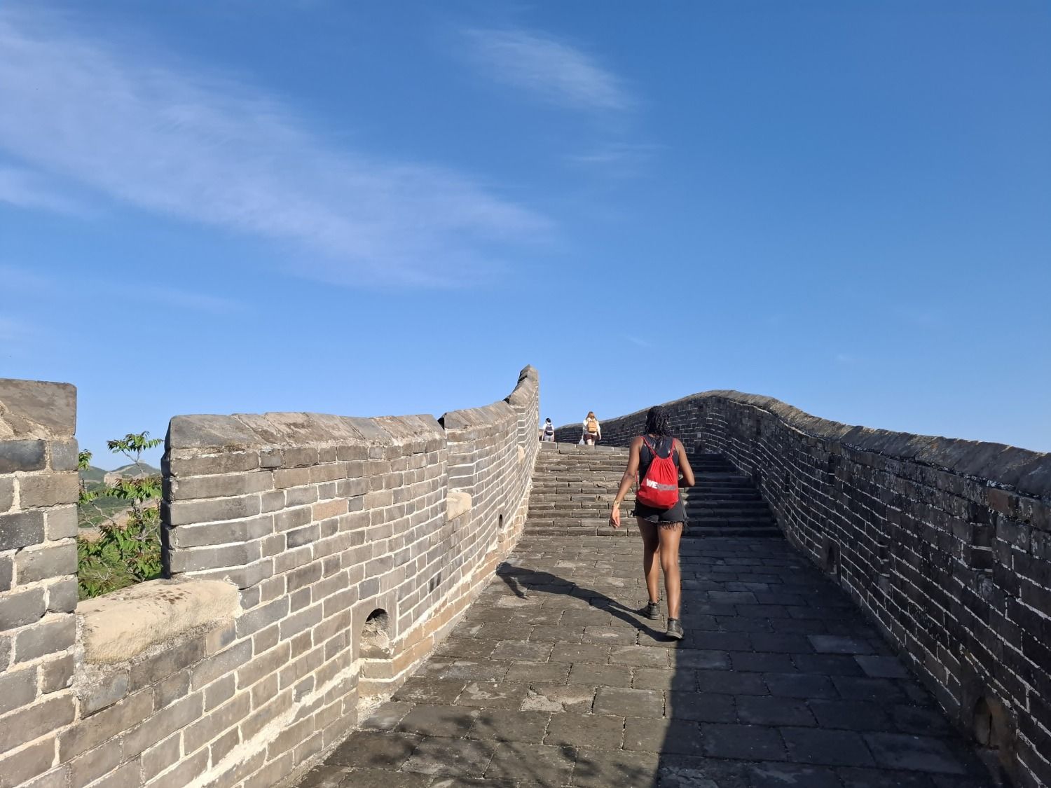Wanderin mit rotem Rucksack auf einem steilen Abschnitt der Chinesischen Mauer.