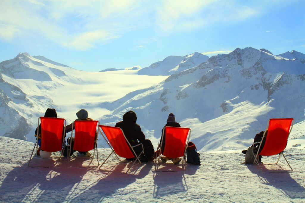 Gruppe entspannt in roten Liegestühlen mit Blick auf ein verschneites Alpenpanorama.