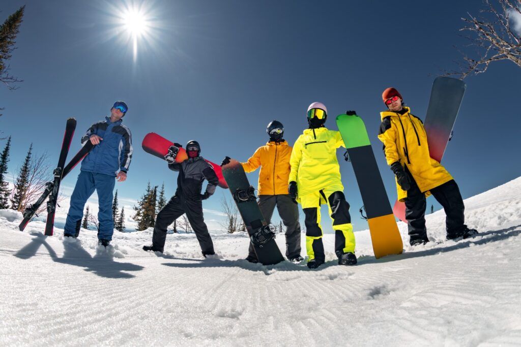 WeRoad Reisegruppe im Skiurlaub mit Skiern und Snowboards vor strahlend blauem Himmel.
